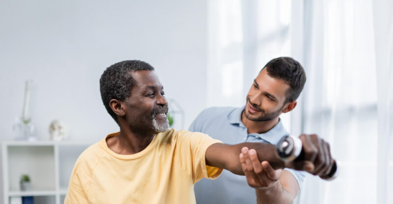 Physiotherapist helping a patient holding a dumbbell